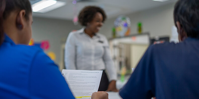 Management careers - Woman standing before two seated people holding a document. | MasterCorp Jobs